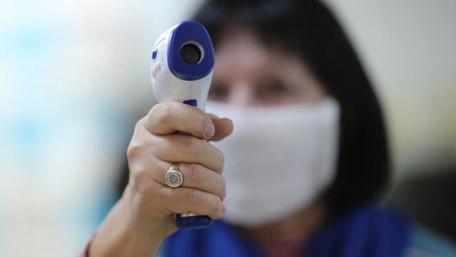 Сотрудница поликлиники готовится измерять температуру посетителей Сотрудница поликлиники готовится измерять температуру посетителей