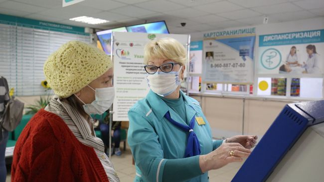 Сотрудница поликлиники  помогает посетительнице получить талон к врачу