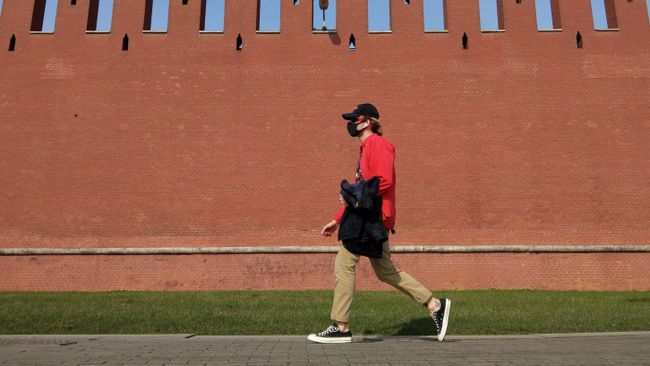 Молодой человек в медицинской маске идет возле Кремлевской стены в Москве