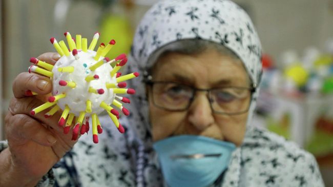 Пожилая женщина в Палестине держит модель клетки коронавируса