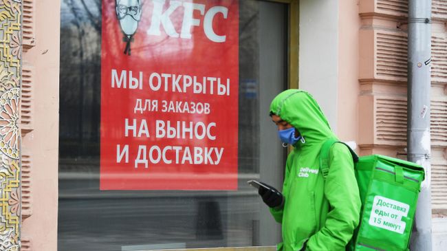 Курьер службы доставки еды Delivery Club стоит в очереди у окна кафе KFC Курьер службы доставки еды Delivery Club стоит в очереди у окна кафе KFC