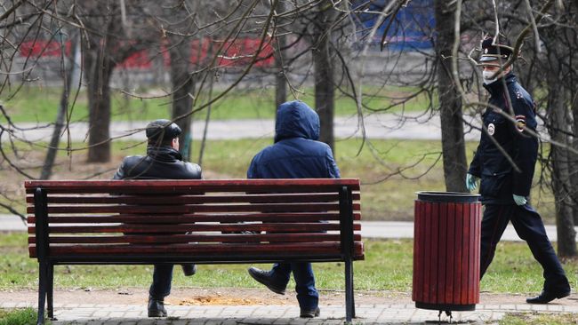 Сотрудник полиции подходит к людям, сидящим на скамейке в сквере Сотрудник полиции подходит к людям, сидящим на скамейке в сквере