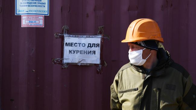 Рабочий в медицинской маске у таблички Место для курения Рабочий в медицинской маске у таблички Место для курения