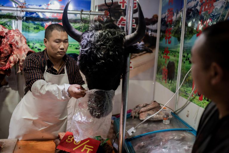 Мясник продает голову яка на рынке в Пекине, Китай Мясник продает голову яка на рынке в Пекине, Китай