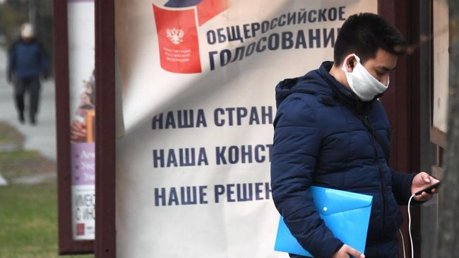Молодой человек в защитной маске стоит у агитационного плаката Молодой человек в защитной маске стоит у агитационного плаката