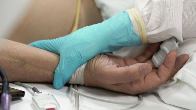 Медицинский работник у постели пациента в стационаре для больных с коронавирусной инфекцией Медицинский работник у постели пациента в стационаре для больных с коронавирусной инфекцией