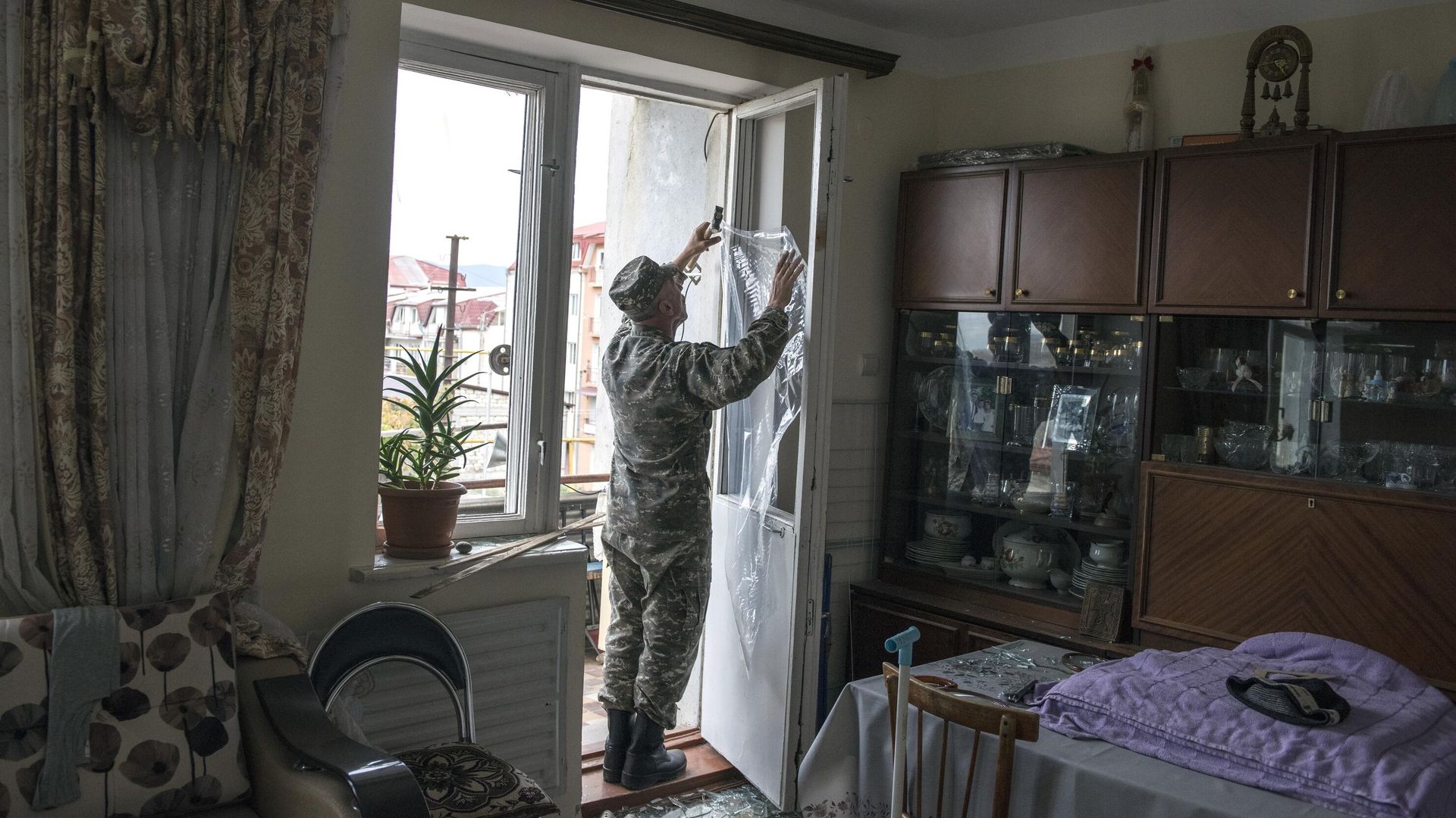 Мужчина закрывает полиэтиленовой пленкой окно с выбитыми стеклами после обстрелов Степанакерта Нагорном Карабахе - РИА Новости, 1920, 12.10.2020