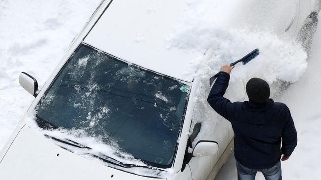 Мужчина сметает снег с машины