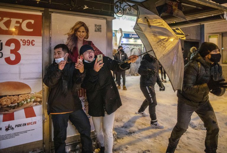 Юноши прячутся за зонтом во время игры в снежки на площади Кальяо в Мадриде Юноши прячутся за зонтом во время игры в снежки на площади Кальяо в Мадриде