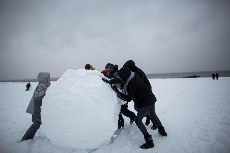 Люди катают снежный ком во время снегопада на Брайтон-Бич в Нью-Йорке Люди катают снежный ком во время снегопада на Брайтон-Бич в Нью-Йорке