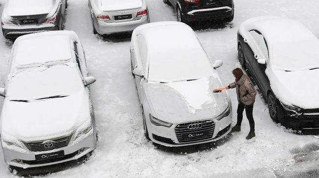 Девушка чистит автомобиль от снега на стоянке 
