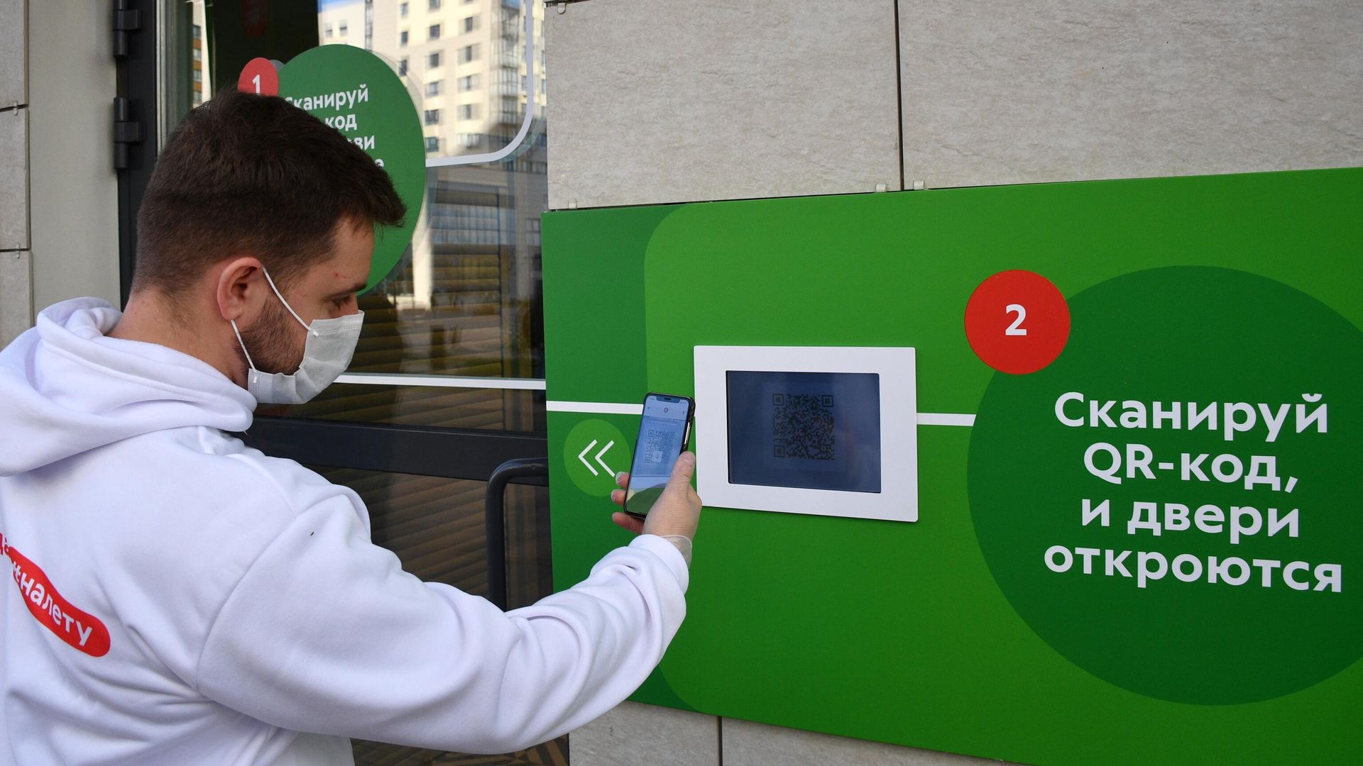 Молодой человек в защитной маске сканирует QR-код с помощью смартфона на входе в магазин Молодой человек в защитной маске сканирует QR-код с помощью смартфона на входе в магазин - РИА Новости, 1920, 28.06.2021