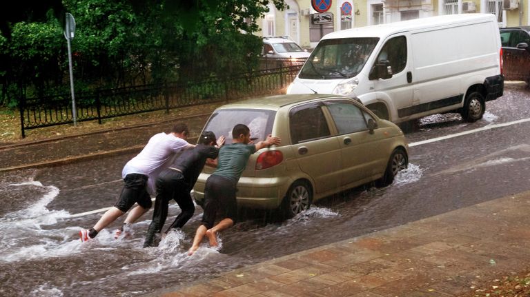 Молодые люди толкают автомобиль на одной из улиц в Москве во время дождя Молодые люди толкают автомобиль на одной из улиц в Москве во время дождя