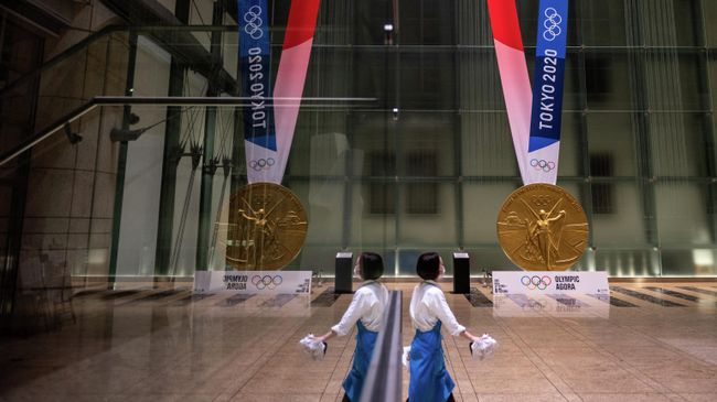 A woman walks near a large-scale reproduction of the Tokyo 2020 Olympic Games gold medal as part of the Olympic Agora event at Mitsui Tower in Tokyo on July 14, 2021. (Photo by Philip FONG / AFP)
