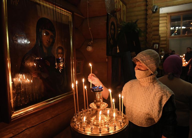 Женщина ставит свечу во время ночной Рождественской службы в православной Знаменской церкви в городе Дивногорске Красноярского края