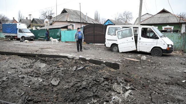 Воронка от взрыва и поврежденный в результате обстрела автомобиль в Киевском районе Донецка