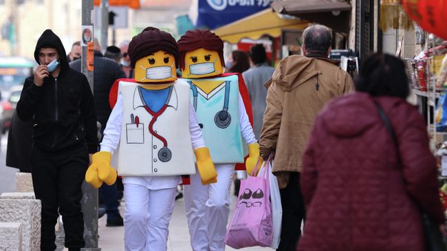 Люди, одетые как фигурки врачей Lego, проходят мимо магазинов в Иерусалиме, за день до еврейского праздника Пурим. Люди, одетые как фигурки врачей Lego, проходят мимо магазинов в Иерусалиме, за день до еврейского праздника Пурим.