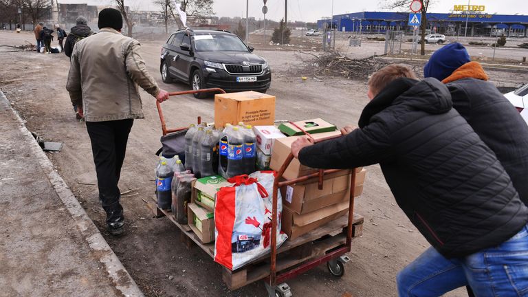Местные жители везут тележку с продуктами возле магазина Metro в Мариуполе Местные жители везут тележку с продуктами возле магазина Metro в Мариуполе