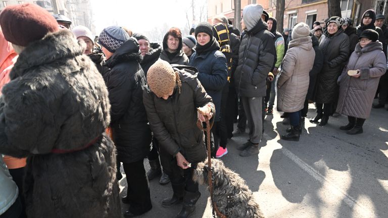 Жители Мариуполя стоят в очереди за гуманитарной помощью от волонтеров. В центре: женщина делится хлебом со своей собакой Жители Мариуполя стоят в очереди за гуманитарной помощью от волонтеров. В центре: женщина делится хлебом со своей собакой