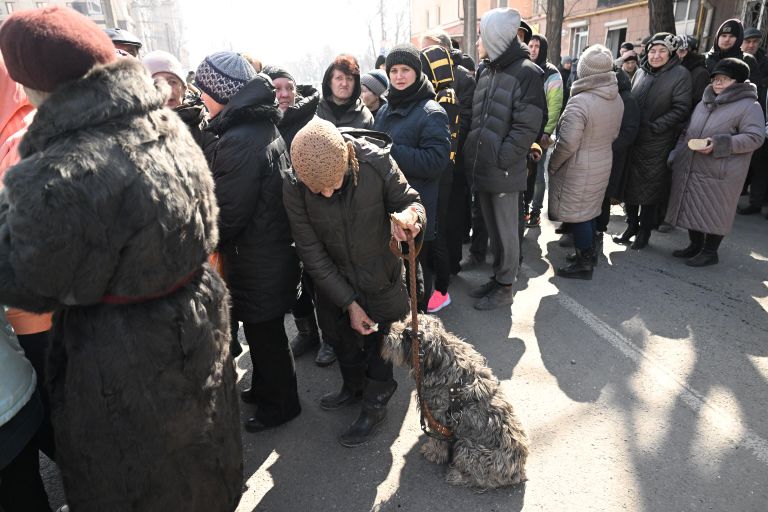 Жители Мариуполя стоят в очереди за гуманитарной помощью от волонтеров. В центре: женщина делится хлебом со своей собакой Жители Мариуполя стоят в очереди за гуманитарной помощью от волонтеров. В центре: женщина делится хлебом со своей собакой
