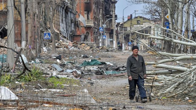 Житель Мариуполя у разрушенных зданий на улице города