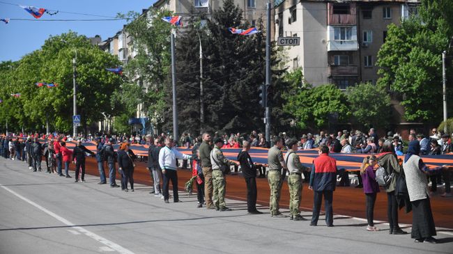 Колонна людей во время шествия с 300-метровой георгиевской лентой в Мариуполе на праздничных мероприятиях
