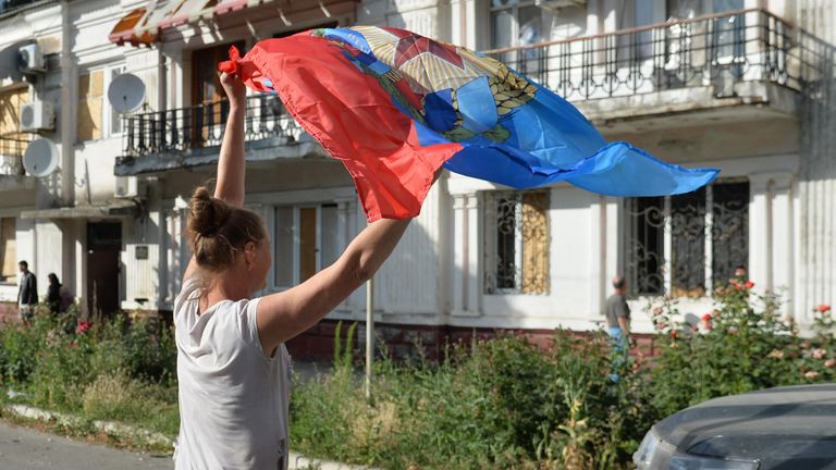 Местная жительница с флагом ЛНР, подаренным бойцами 6-го казачего полка имени Платова ЛНР и специального полка полиции имени Героя России Ахмата-Хаджи Кадырова у здания администрации в Лисичанске Местная жительница с флагом ЛНР, подаренным бойцами 6-го казачего полка имени Платова ЛНР и специального полка полиции имени Героя России Ахмата-Хаджи Кадырова у здания администрации в Лисичанске