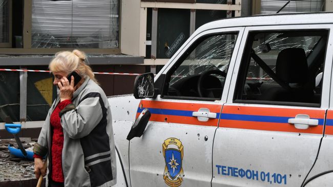 Женщина возле машины МЧС после обстрела