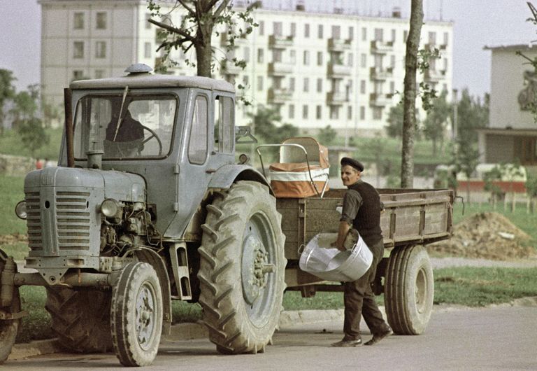 Молодой папа грузит на прицеп трактора детские вещи Молодой папа грузит на прицеп трактора детские вещи