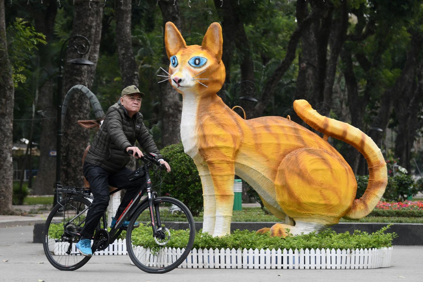 Мужчина проезжает возле статуи кошки в парке Thong Nhat Park  в Ханое, Вьетнам