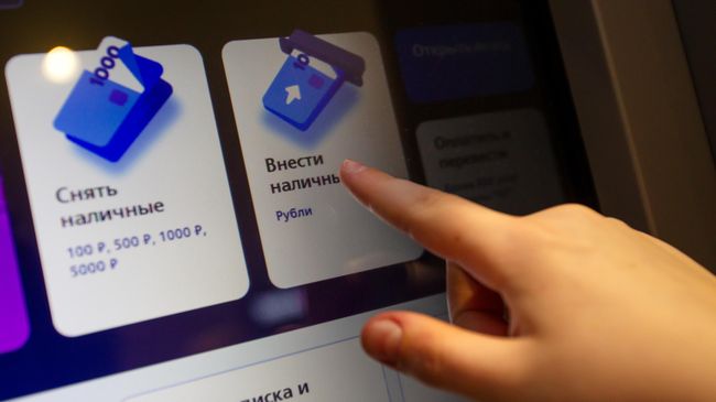 Посетитель кладет деньги на банковский счет в банкомате