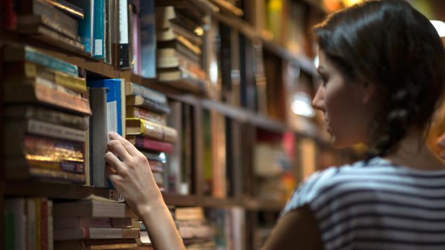 Девушка выбирает книгу в библиотеке