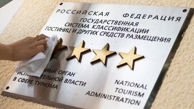 Сотрудница санатория в Сочи чистит табличку звездности на здании отеля