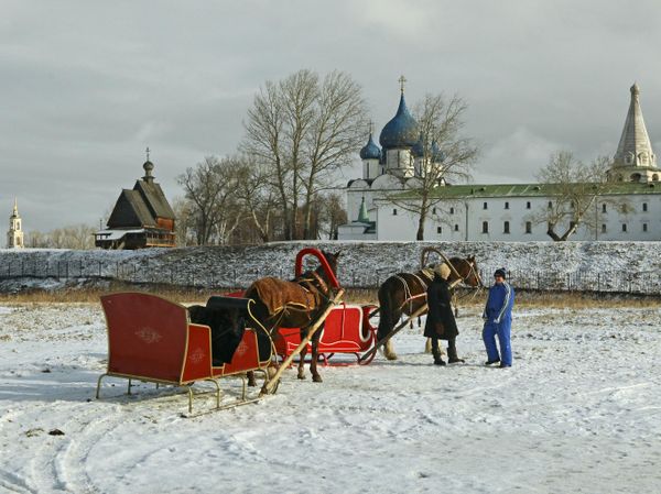 Запряженные лошадьми сани на фоне Суздальского кремля и деревянной церкви Николая Чудотворца Запряженные лошадьми сани на фоне Суздальского кремля и деревянной церкви Николая Чудотворца