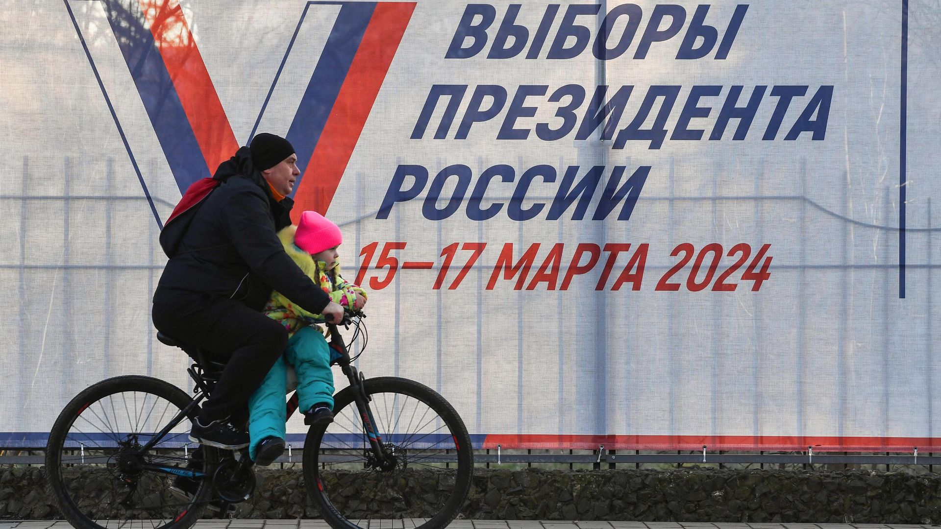 Мужчина с ребенком на велосипеде у предвыборного плаката на одной из улиц города Саки - РИА Новости, 1920, 21.02.2024