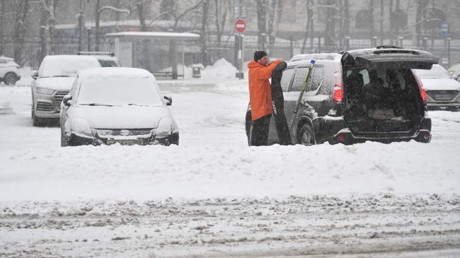 Мужчина стоит возле своей машины во время снегопада в Москве