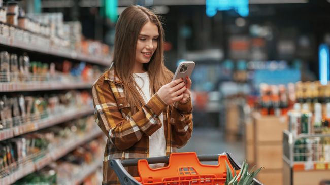 Девушка использует смартфон в супермаркете