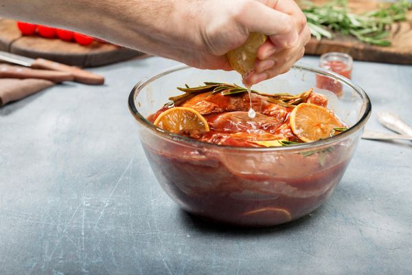 Мужчина выжимает сок лимона в мясо в маринаде