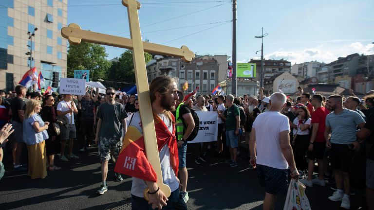 Молодой человек несет деревянный крест на плече на площади Славия в Белграде во время акции протеста