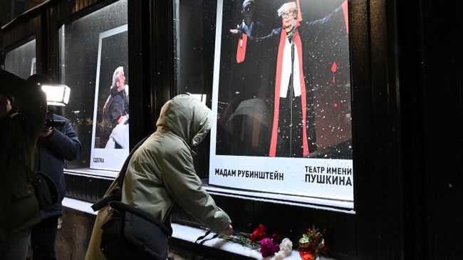 Женщина оставляет цветы у афиши спектакля Мадам Рубинштейн в Театре имени Пушкина