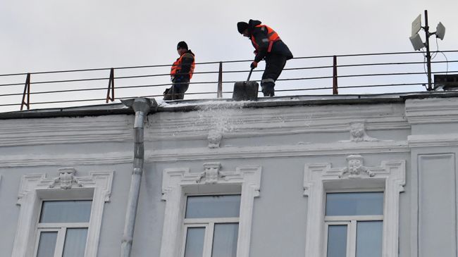 Сотрудники коммунальной службы во время уборки снега с крыши дома в Москве. 