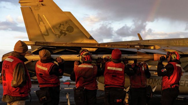 Военнослужащие ВМС США загружают боеприпасы на истребитель F/A-18E Super Hornet на палубе авианосца USS Gerald R. Ford во время операции Эпическая ярость