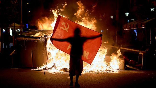 Протестующий держит флаг рядом с горящими мусорными баками во время столкновений с полицией