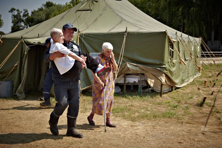 Сотрудник МЧС Украины переносит пожилую женщину, приехавшую из зоны силовой операции киевских властей на востоке Украины Сотрудник МЧС Украины переносит пожилую женщину, приехавшую из зоны силовой операции киевских властей на востоке Украины