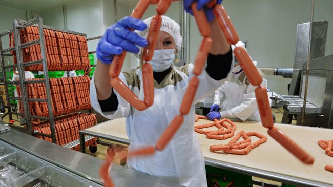 Рабочий упаковывает продукцию на фабрике мясной гастрономии. Архивное фото Рабочий упаковывает продукцию на фабрике мясной гастрономии. Архивное фото