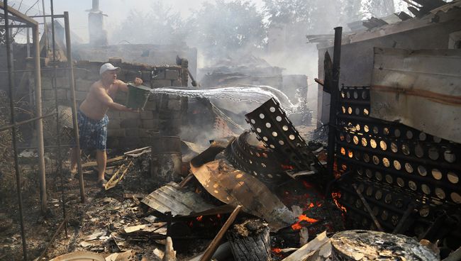 Житель Донецка тушит пожар в своем доме после обстрела Житель Донецка тушит пожар в своем доме после обстрела