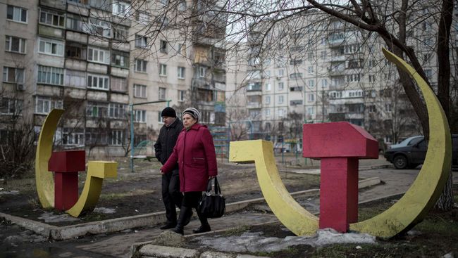 Местные жители проходят мимо скульптур серпа и молота в Мариуполе, Украина