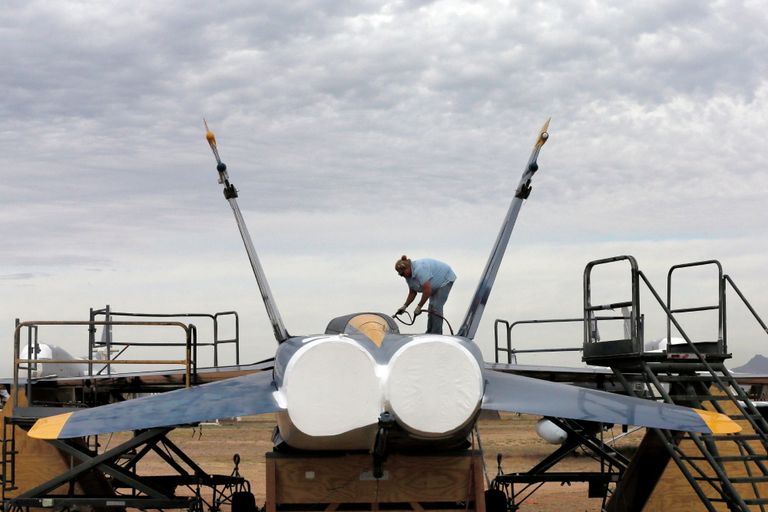 Военнослужащий покрывает водонепроницаемой краской американский истребитель-бомбардировщик F-18 на авиабазе ВВС США Девис-Монтен в Тусоне, Аризона Военнослужащий покрывает водонепроницаемой краской американский истребитель-бомбардировщик F-18 на авиабазе ВВС США Девис-Монтен в Тусоне, Аризона