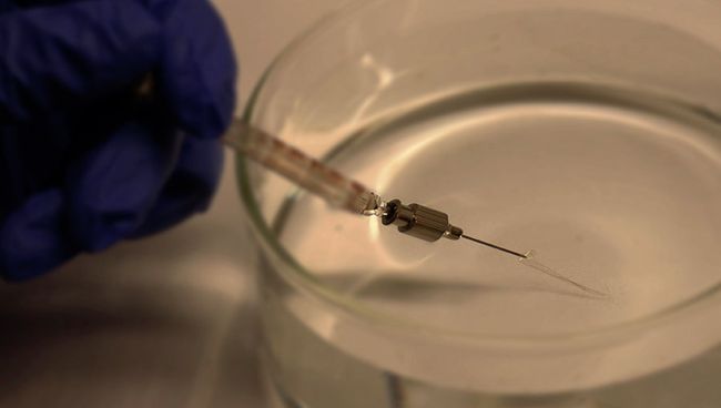 Экспериментатор выдавливает сетку из шприца в медицинский раствор Экспериментатор выдавливает сетку из шприца в медицинский раствор