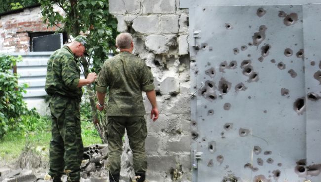 Сотрудники МЧС у ворот, поврежденных осколками в результате обстрела Донецка Сотрудники МЧС у ворот, поврежденных осколками в результате обстрела Донецка